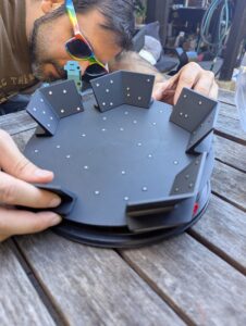 a guy in rainbow sunglasses bending over a scanning turntable to adjust it