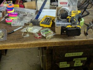 workbench covered with tools and bolts, with drawers labelled "hooks", "sandpaper", "lockpicks" and so on.