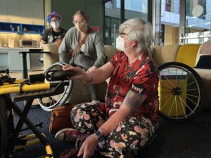 woman wearing a mask with tools working on a manual wheelchair with its rider consulting