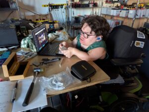 a person seated at laptop with circuit board equipment around them