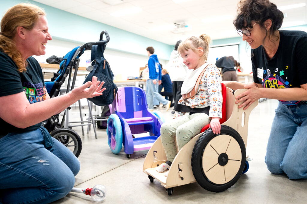 kid and mom smiling while dana adjusts part of the plywood wheelchair
