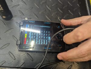 view of a hand, a wire, and a powerchair joystick controller display showing configuration options