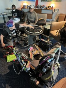 overhead shot of liz on the floor with the manual chair and its stuck wheel, empty powerchair in foreground