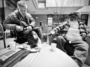 two men, friends from the plaza, sit on the patio recharging their powerchairs and phones