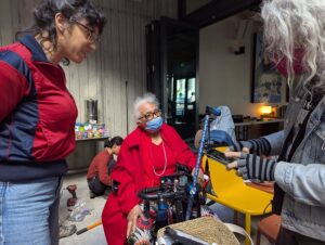 stef opening up the control panel of louetta's scooter as she watches with dana, standing