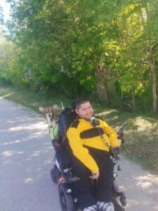 man in powerchair wearing a bright yellow jacket, dog in his backpack