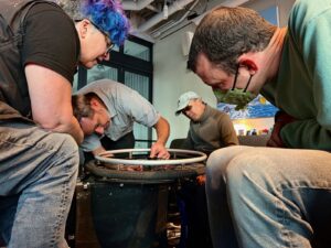 several people bending over a manual chair on its side