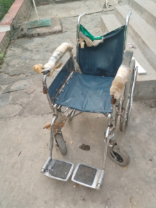 Old manual wheelchair in heavily worn condition with torn upholstery and damaged armrests