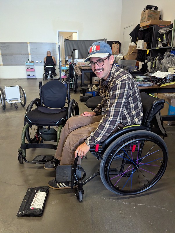 a man in a plaid shirt smiling as he works on a manual wheelchair