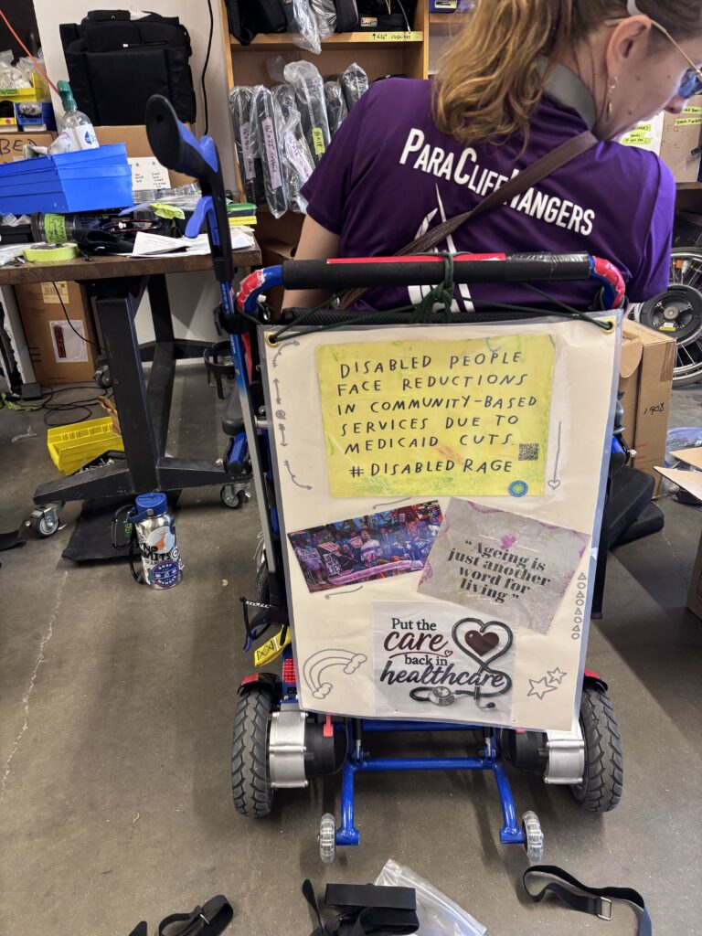 powerchair user with a large sign on back of their chair with activist messages about medicare and health care for disabled people