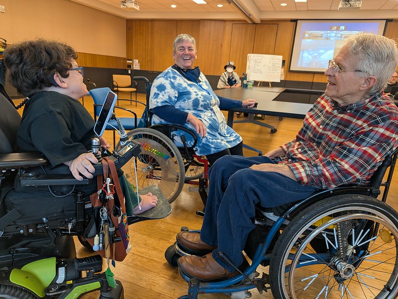 three people in wheelchairs chatting animatedly in a conference room