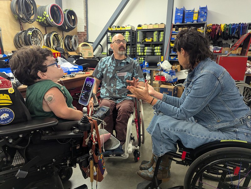two wheelchair users, talking with dana, workshop background