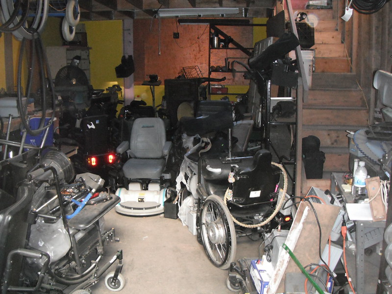 a bunch of old messed up powerchairs in a grungy workshop