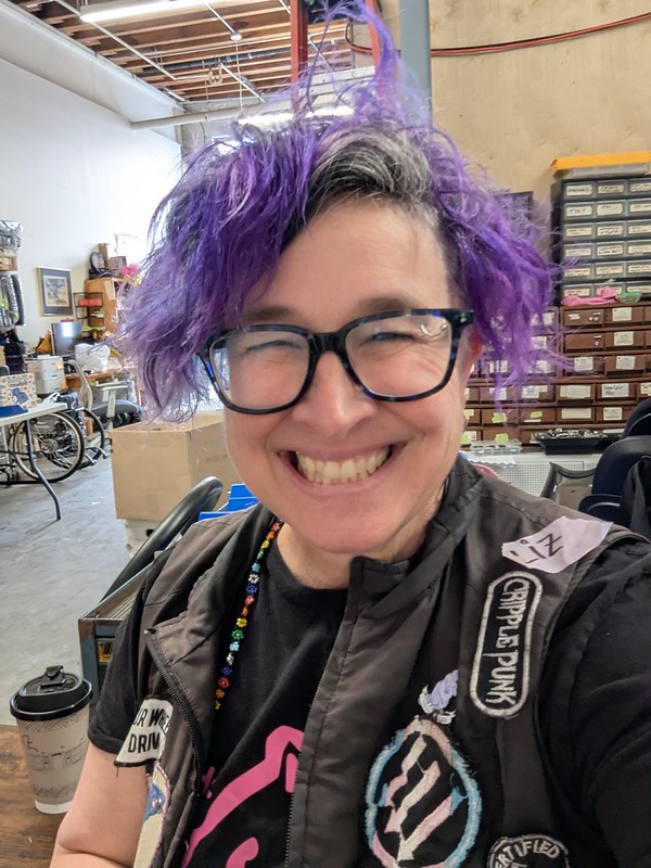 nonbinary white wheelchair user grinning happily in the workshop
