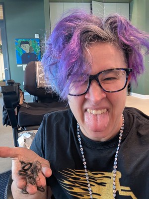 white nonbinary person with purple hair and glasses , tongue out, holding out a gross tangle of hair