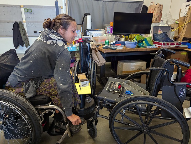 a woman in a manual wheelchair leaning over another broken one