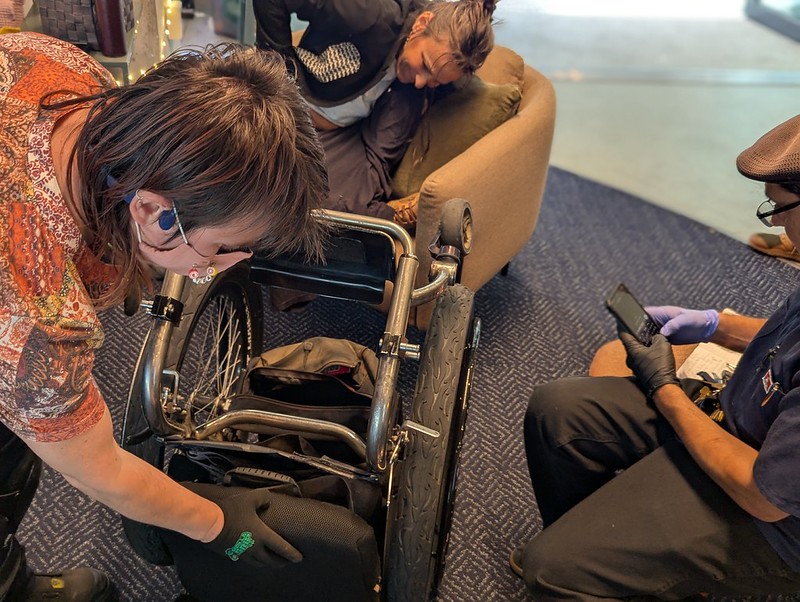two people leaning over a half disassembled wheelchair with large sporty tires