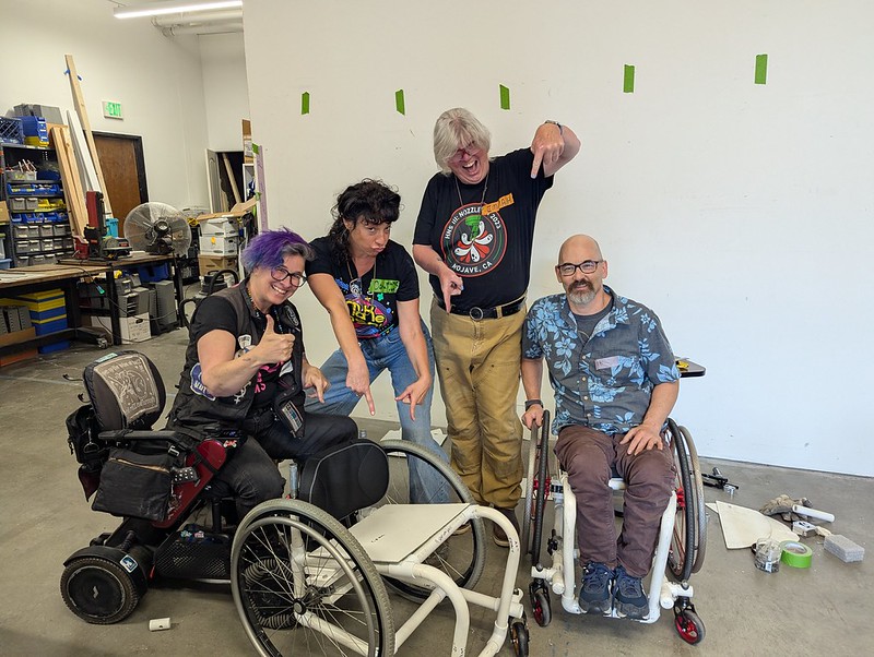 crew of people pointing happily at a just assembled wheelchair made from PVC pipe