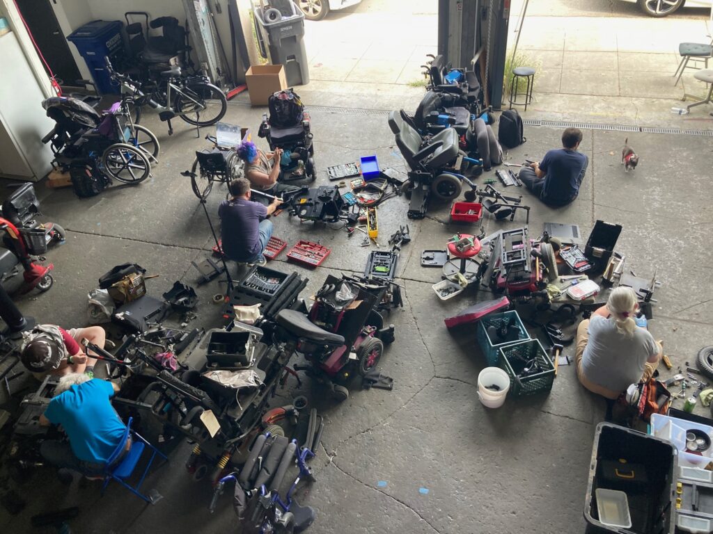 overhead shot of several people on the floor surrounded by tools and half taken apart powerchairs