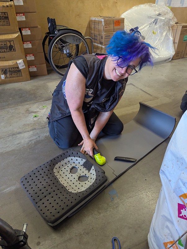 purple haired person on the floor smiling while doing surgery on a cushion
