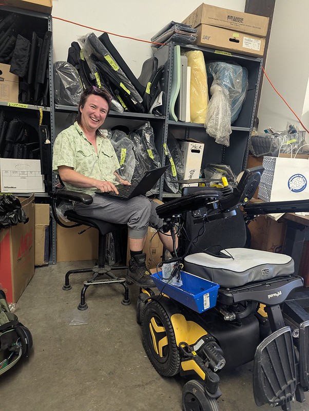 Smiling person sitting with a powerchair in a workshop